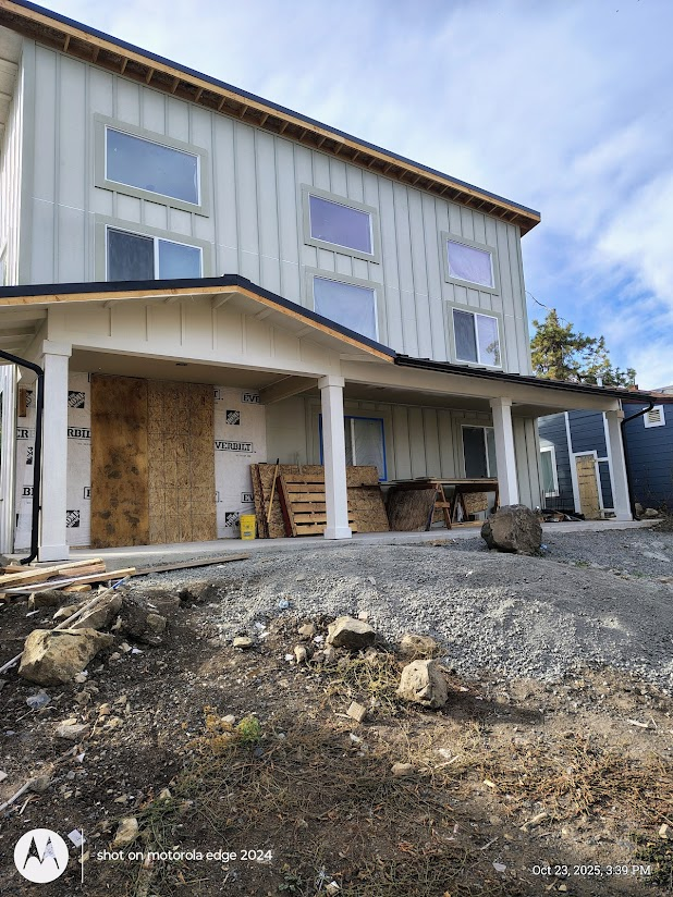 Two-story house under construction. Light grey siding, white trim, covered porch with columns, blue sky.