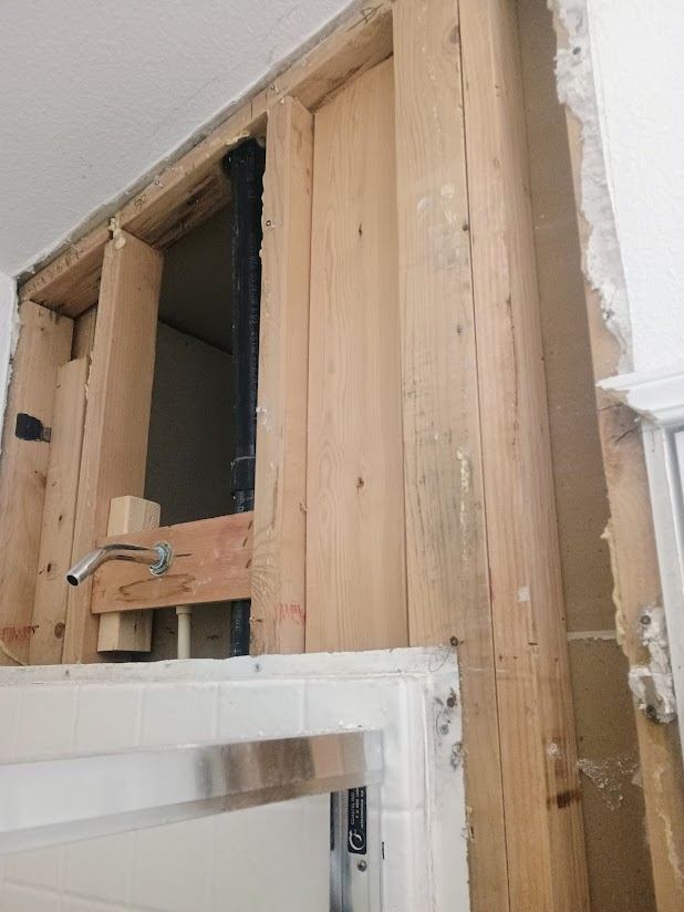Wooden framing around a bathtub and exposed plumbing; the wall is partially demolished.