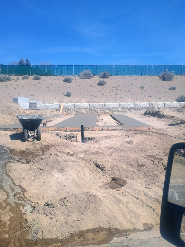 Construction site with concrete work, wheelbarrow, and desert landscape under a blue sky.