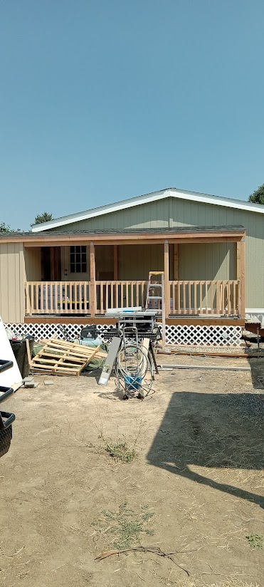 Mobile home with a new wooden porch under a blue sky. Construction tools scattered on the ground.
