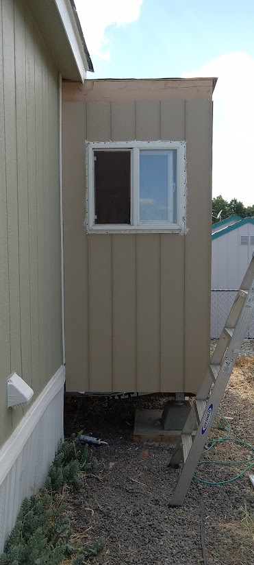 A small structure with a window is attached to a building. A ladder leans against the structure.