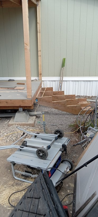 Construction site with a partially built porch and steps. A table saw is in the foreground.