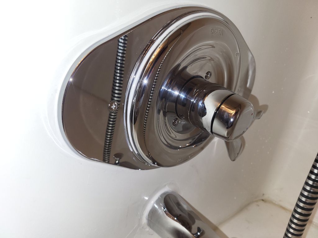 Chrome shower faucet and control knob on a white tub wall