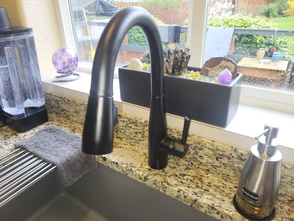 Black kitchen faucet by window over granite sink, with soap dispenser and dish rack on counter