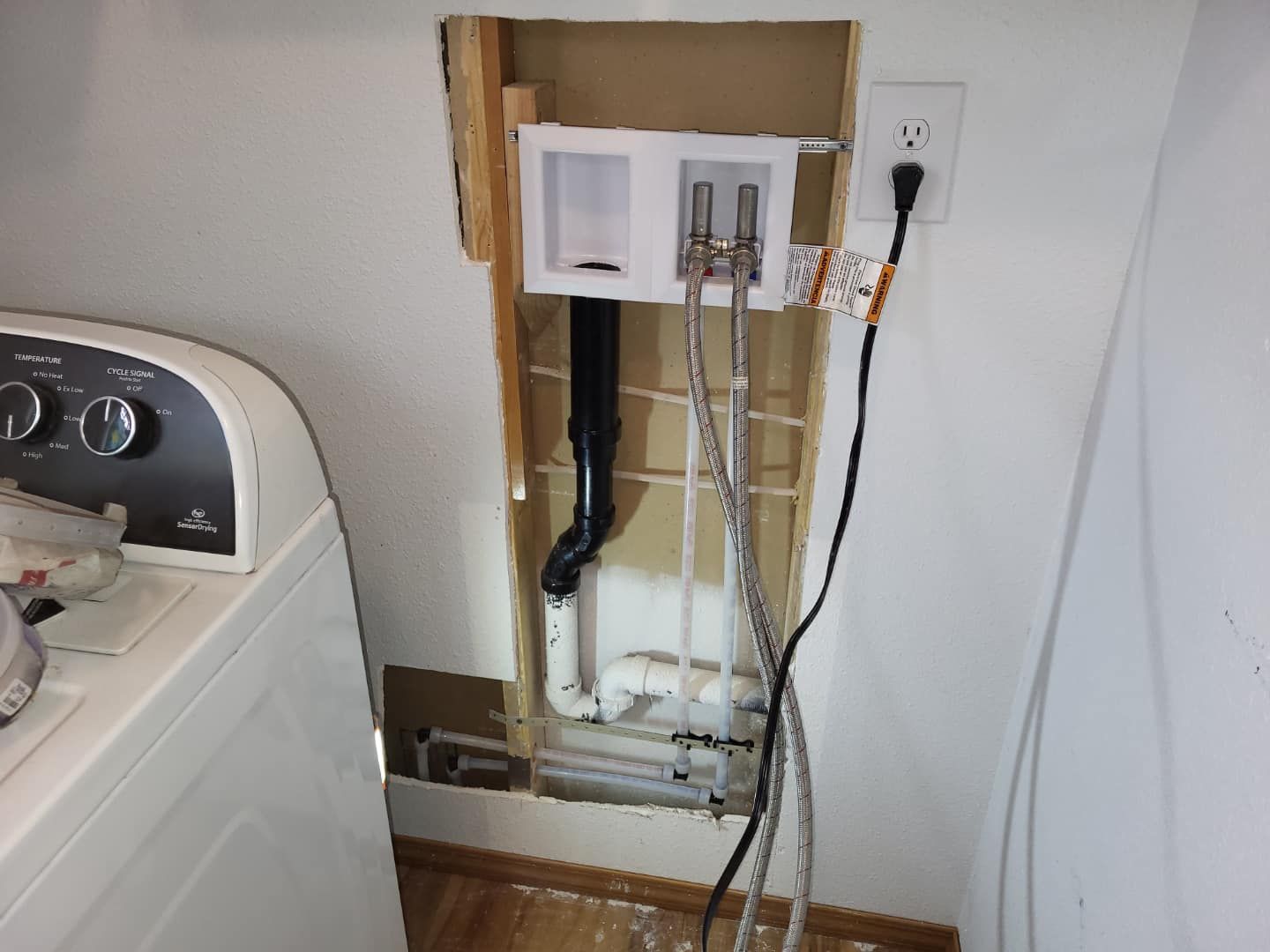 A washer and dryer in a laundry room with a hole in the wall
