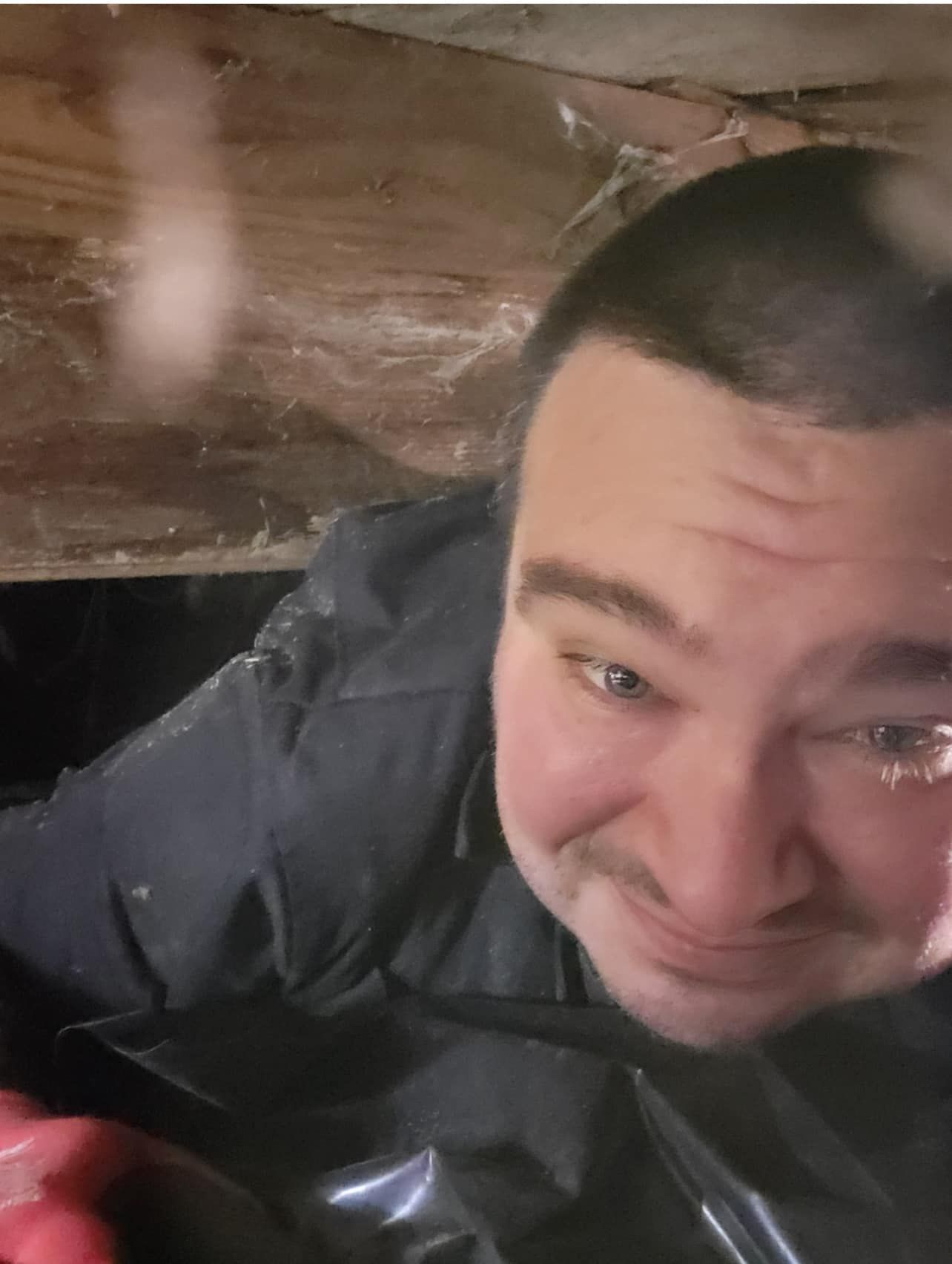A man is crawling under a wooden beam.