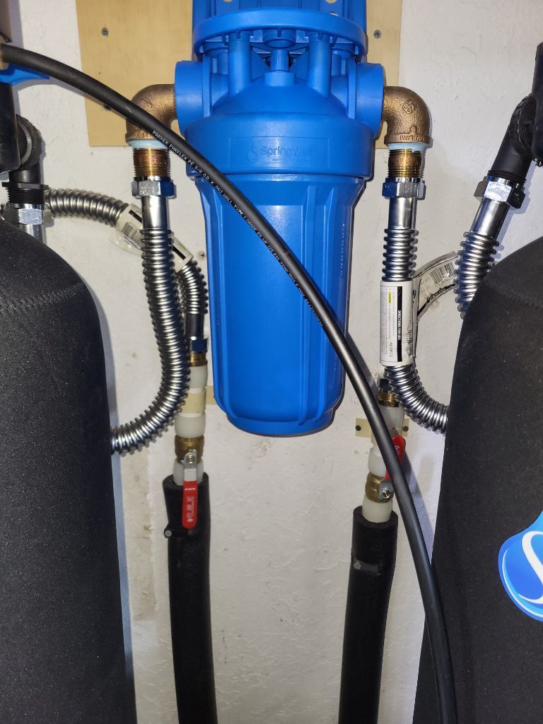 Blue water filter canister with hoses and fittings installed between two black tanks.