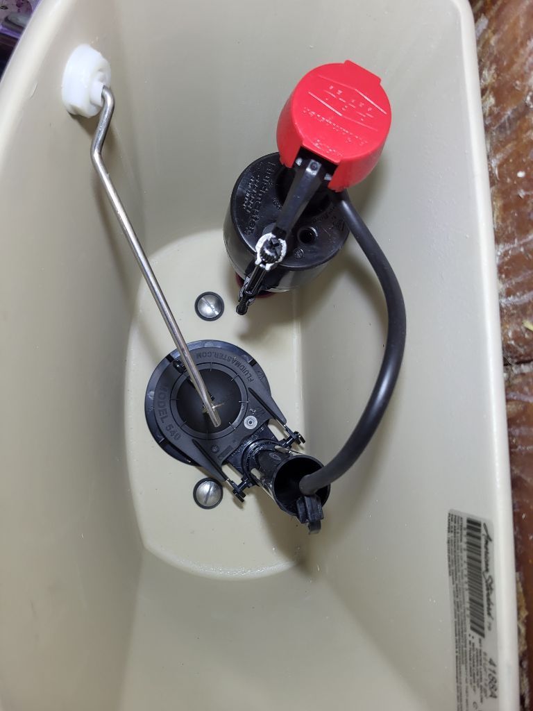 Inside a beige tank, two toilet fill valves with black hoses and red and black caps mounted on the wall.