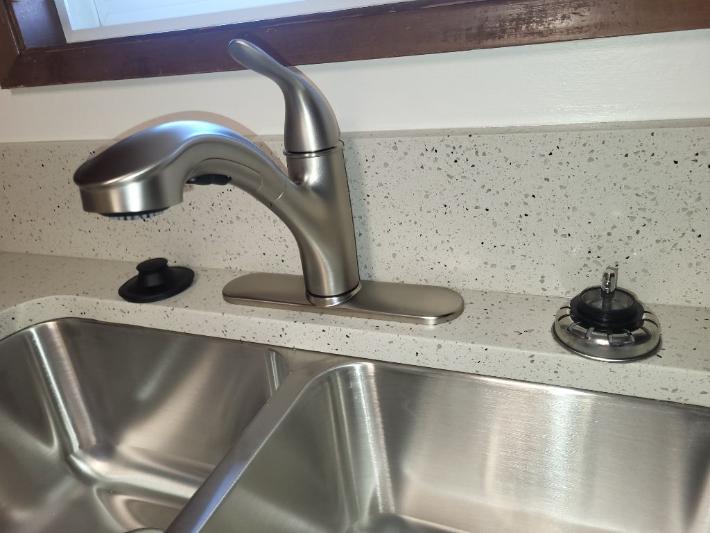 Stainless steel kitchen sink with brushed nickel faucet and speckled countertop, with soap dispensers on each side