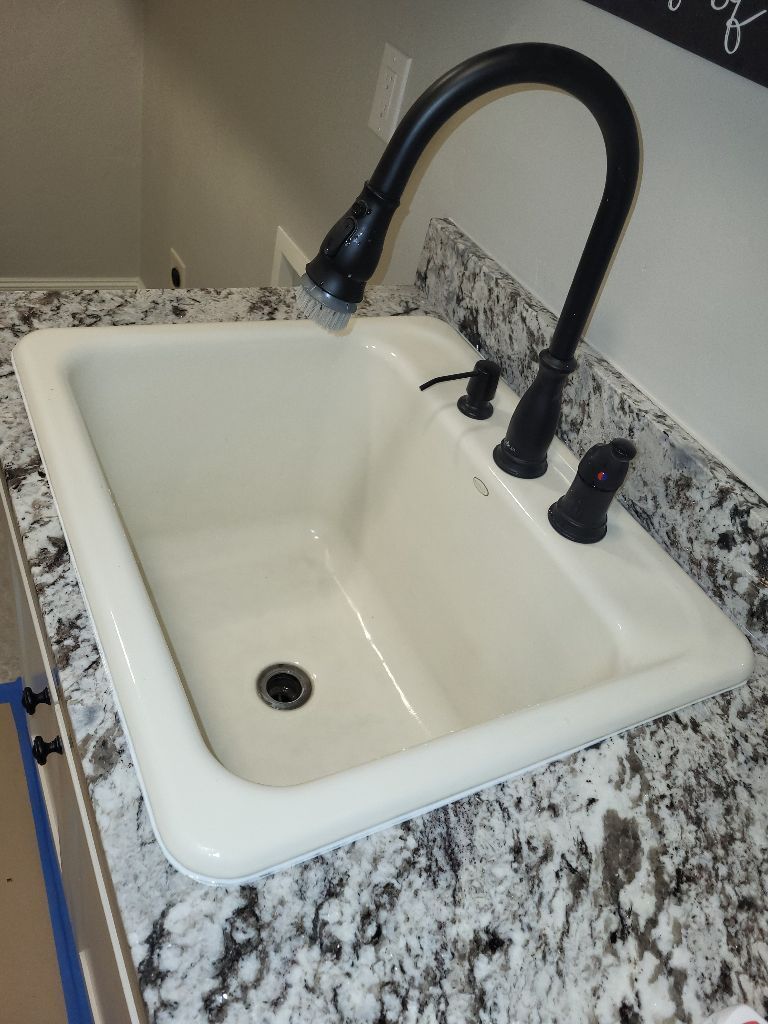 White utility sink with black gooseneck faucet on a speckled granite countertop.
