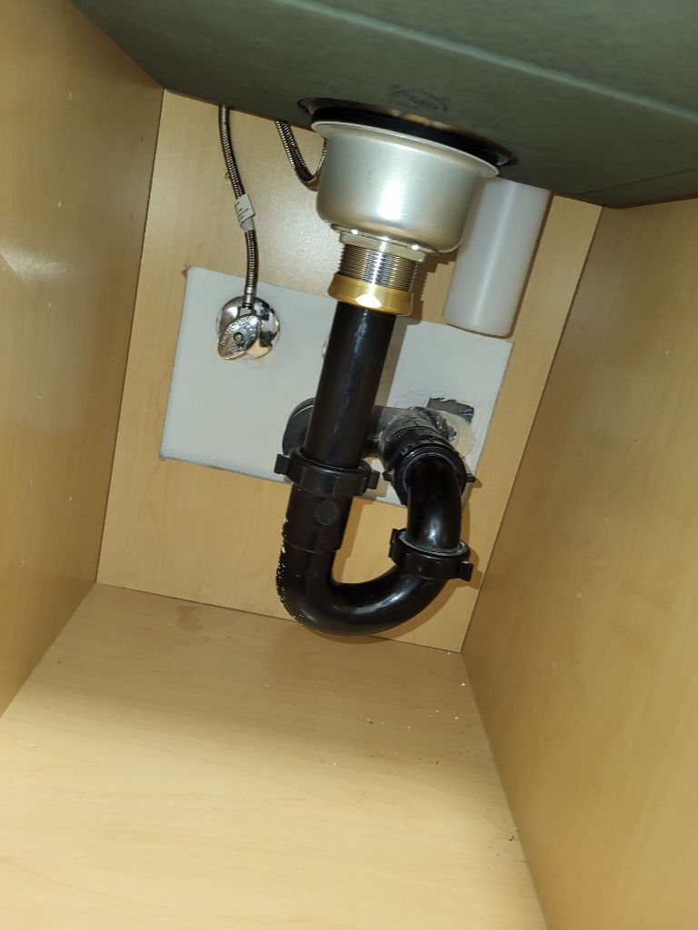 Under-sink plumbing with a black P-trap and metal drain pipe inside a cabinet