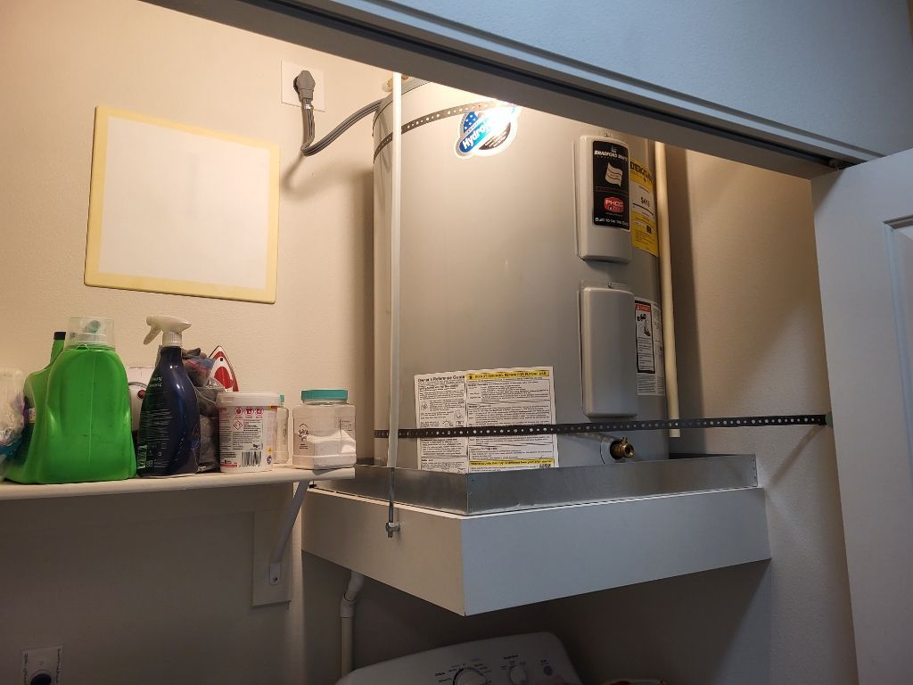 Laundry room with washer, detergent bottles, utility sink, and a wall-mounted water heater