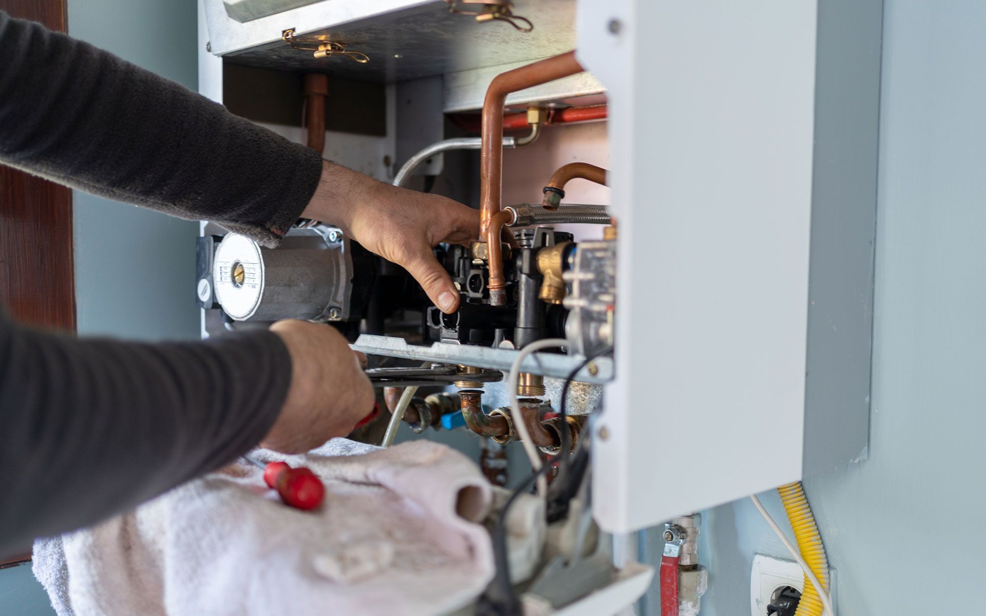 A man is fixing a boiler with a wrench.