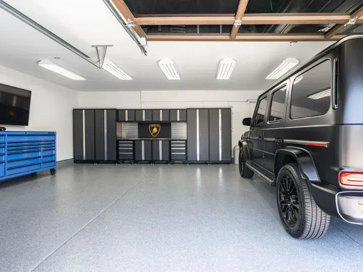 A well-lit garage with a black SUV, cabinets, and a blue tool chest.