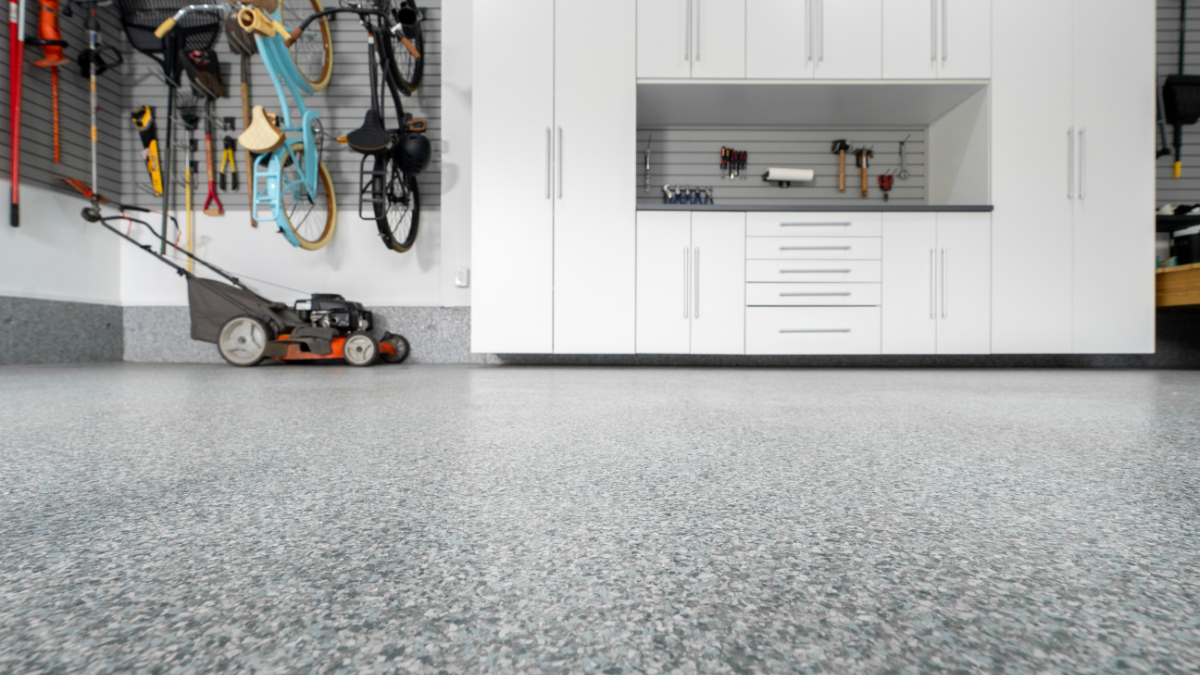 Shiny gray industrial floor reflecting the interior of a warehouse with open doors and bright lighting.