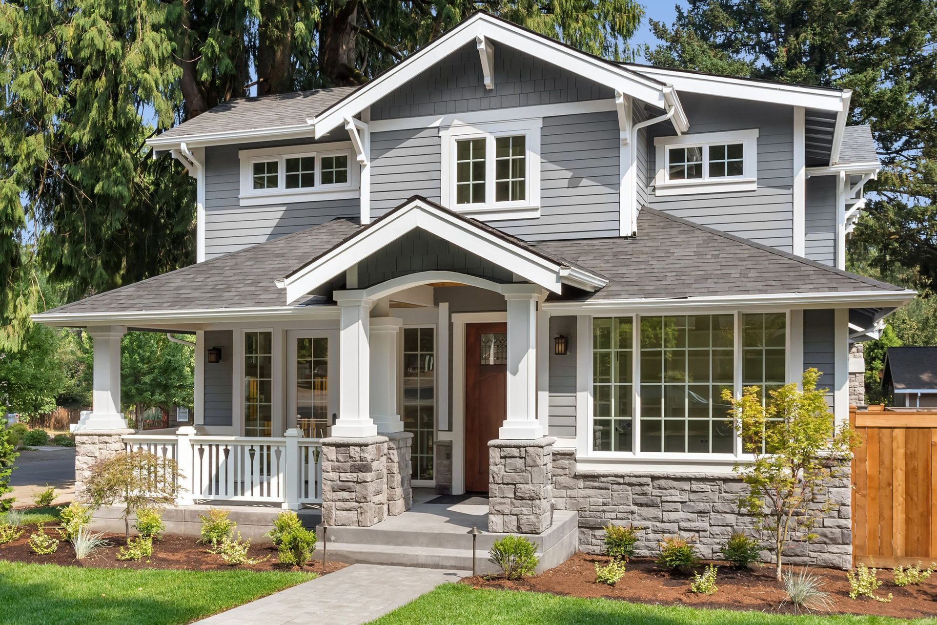 A large gray and white house with a large porch and lots of windows.
