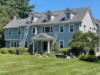 A large blue house with a gray roof is being painted.