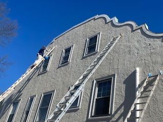 A man is painting the side of a building with a ladder.