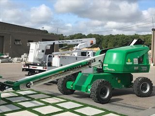 A green aerial lift is parked in front of a building.