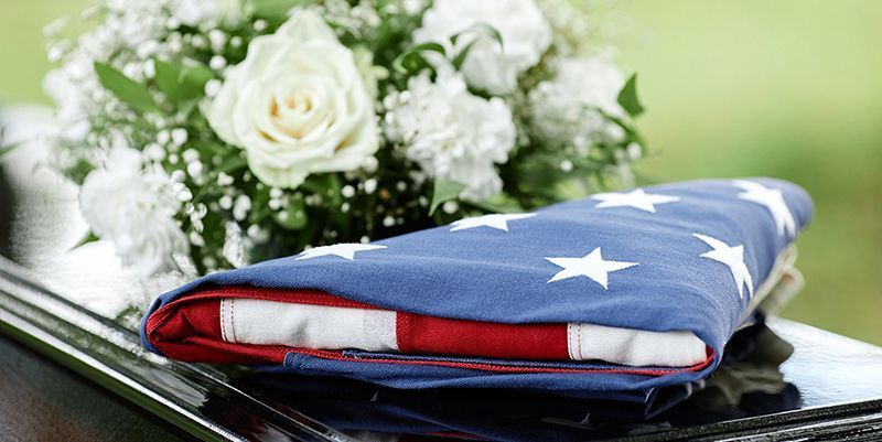 An american flag is laying on top of a limousine next to a bouquet of flowers.