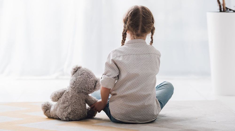 A little girl is sitting on the floor holding a teddy bear.