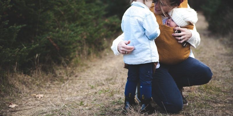 A woman is kneeling down with two children in a field.