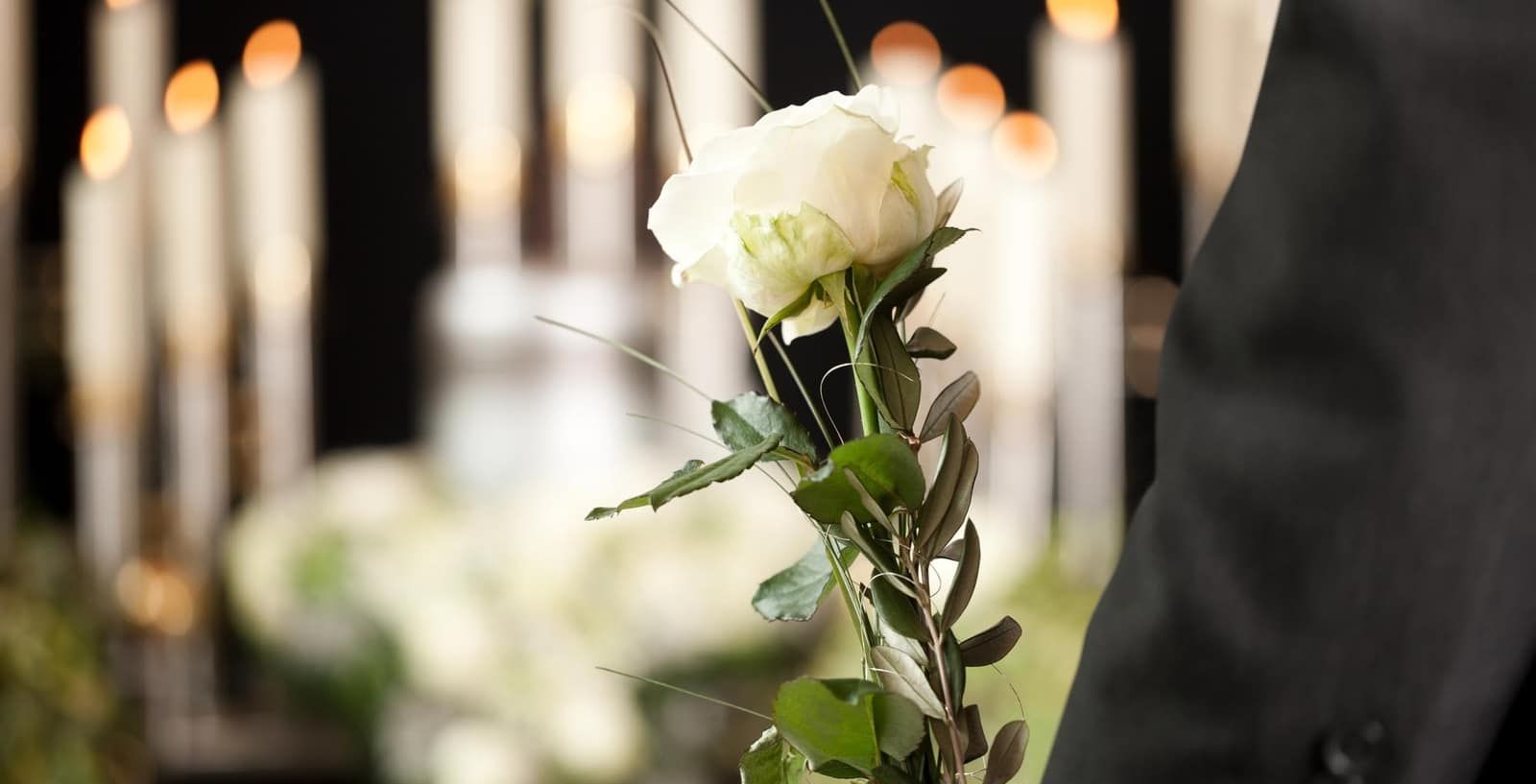 A man in a suit is holding a white rose at a funeral.