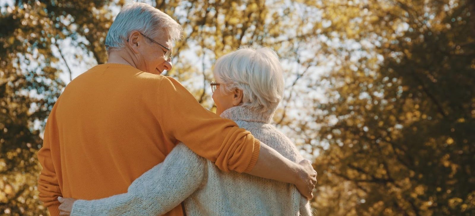 An elderly couple standing next to each other in a park.