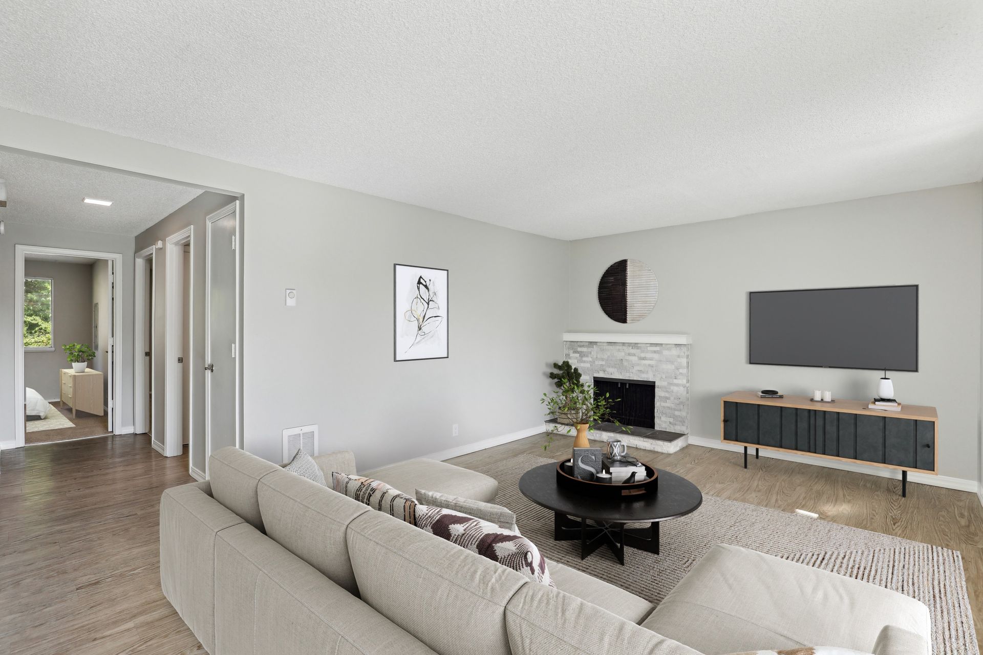 Living room with beige sectional sofa, round black coffee table, stone fireplace, and wall-mounted TV.