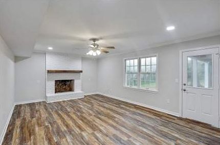 A living room with hardwood floors , a fireplace , and a ceiling fan.