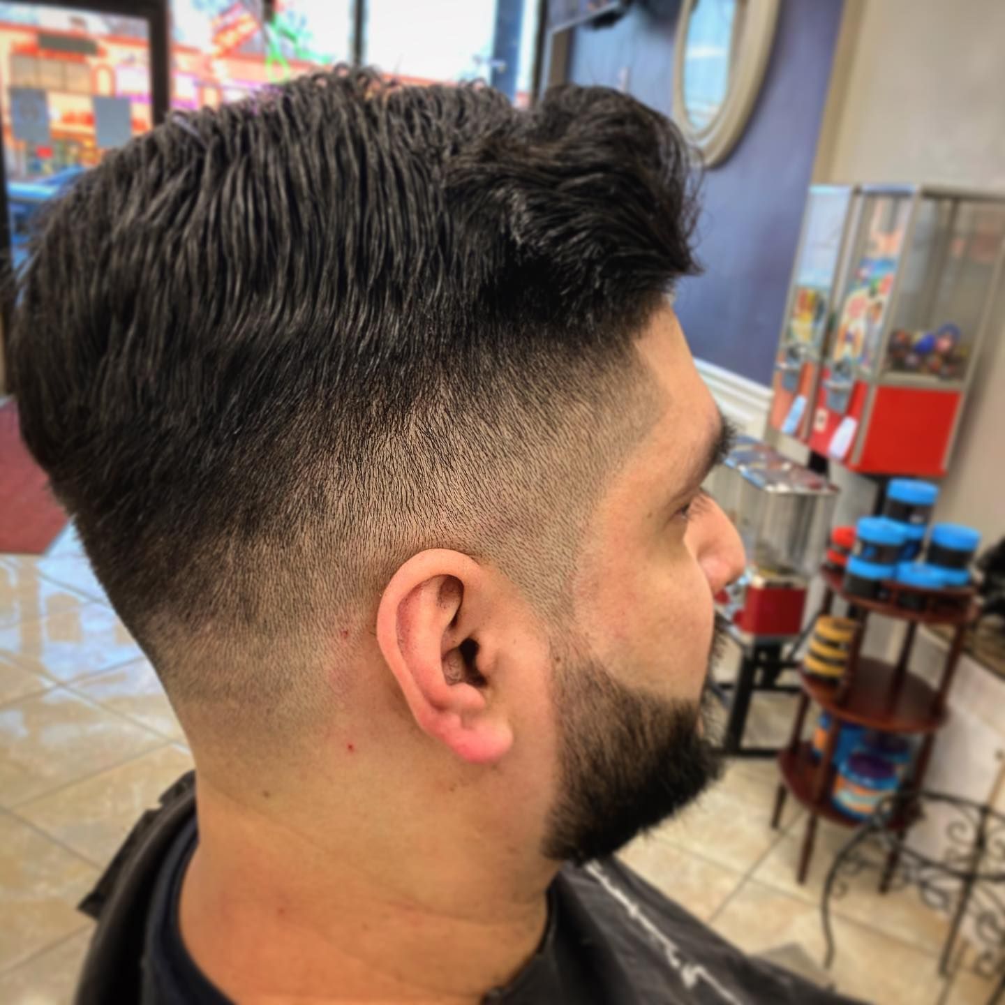 Man with a faded haircut and beard, in a barbershop.