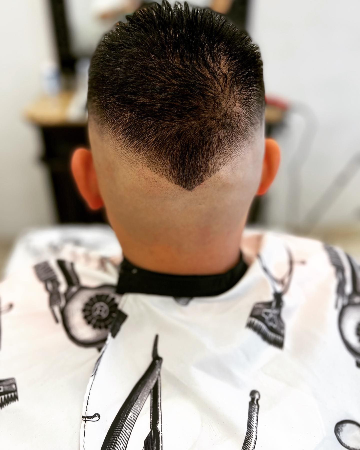 A person with a close-cropped haircut featuring a V-shaped design at the neckline.