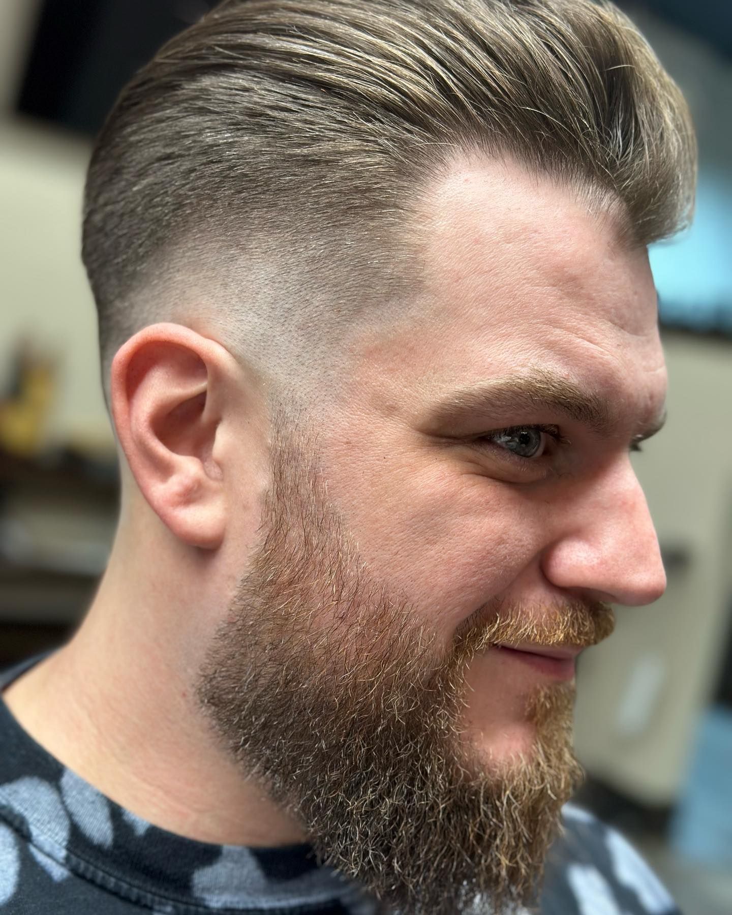 Man with faded haircut and beard, looking right, smiling, indoors.