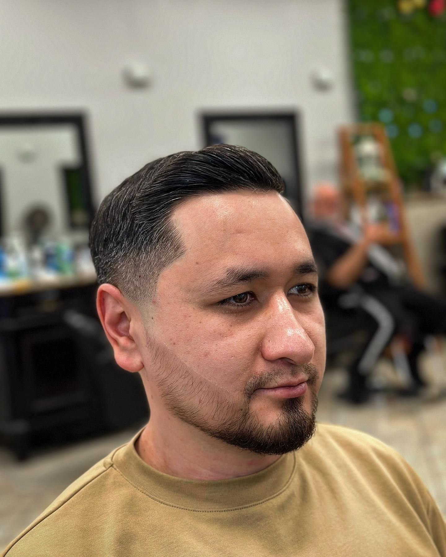 Man with fade haircut and beard, in a salon, looking to the right.