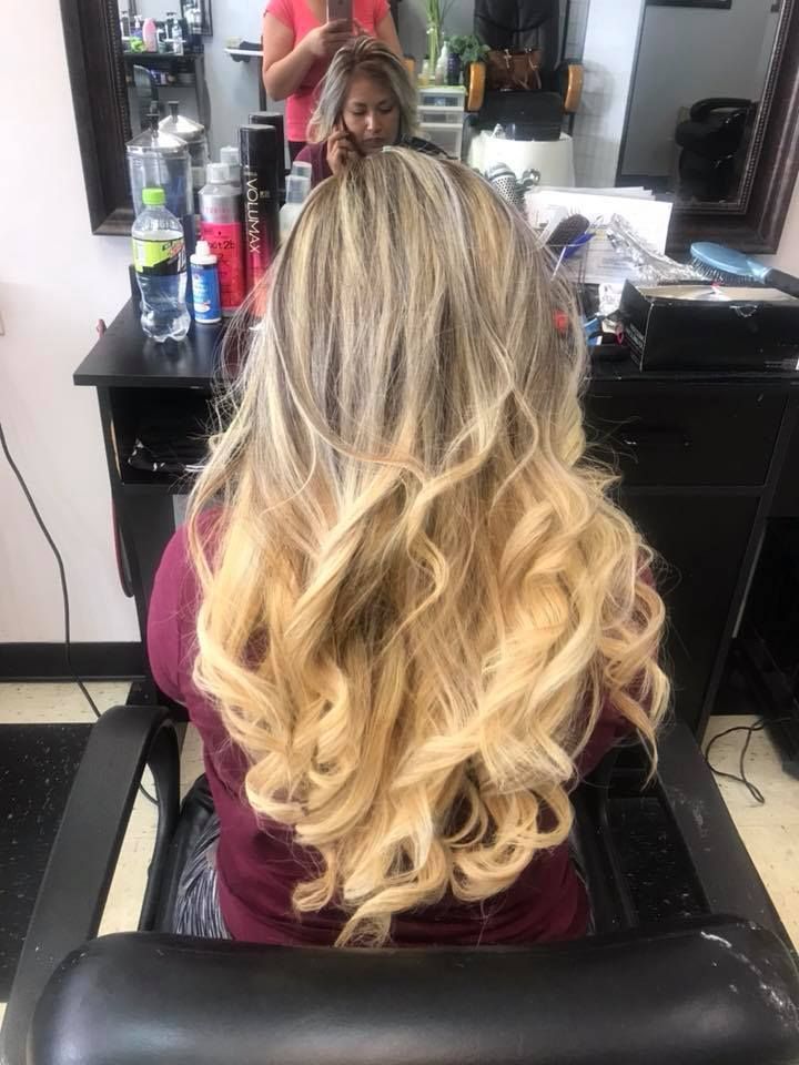 Woman in salon chair with long wavy blonde hair, getting a haircut.
