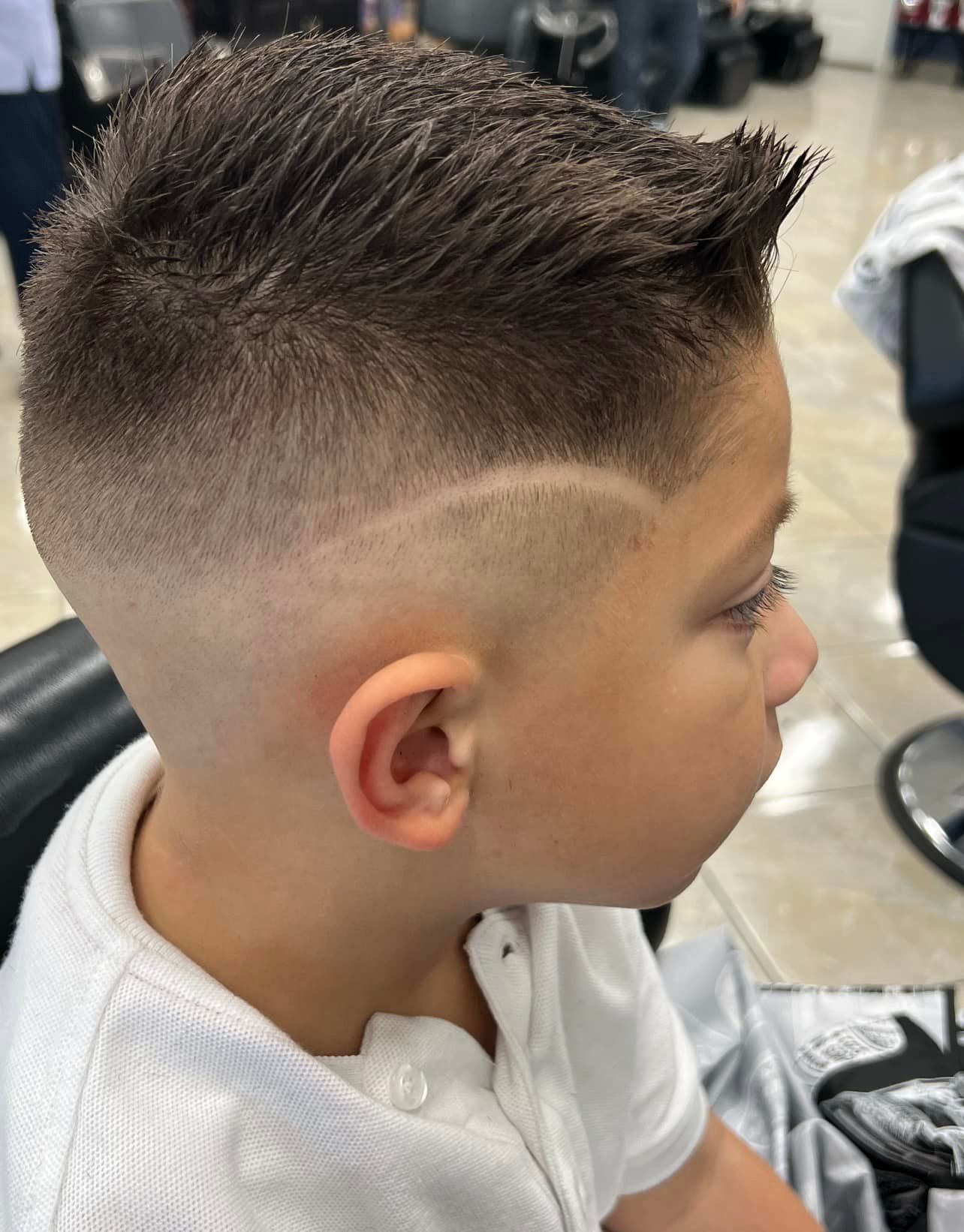 Boy with faded haircut, side part with a line, wearing a white shirt, in a barber shop.