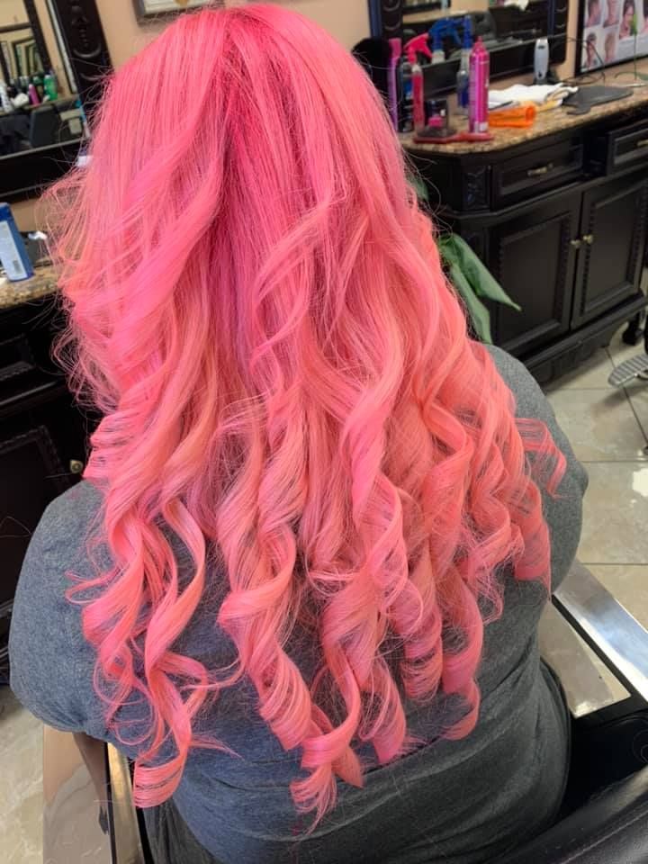 Woman with long, pink, curly hair sitting in a salon chair.