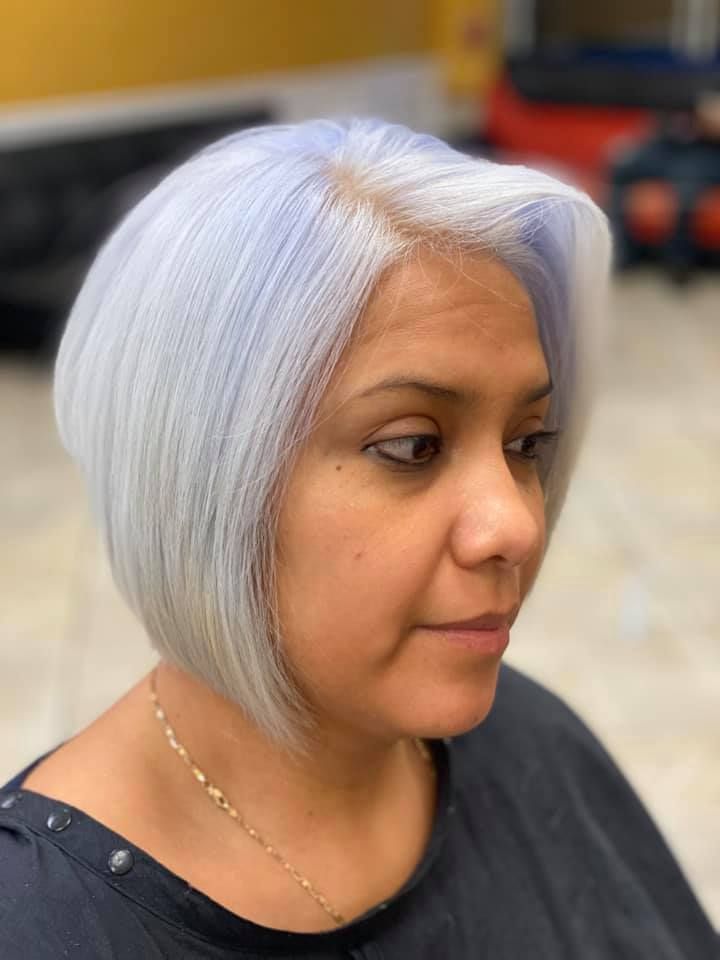 Woman with a short, silver bob haircut and a touch of blue. She's wearing a black top and a gold chain.