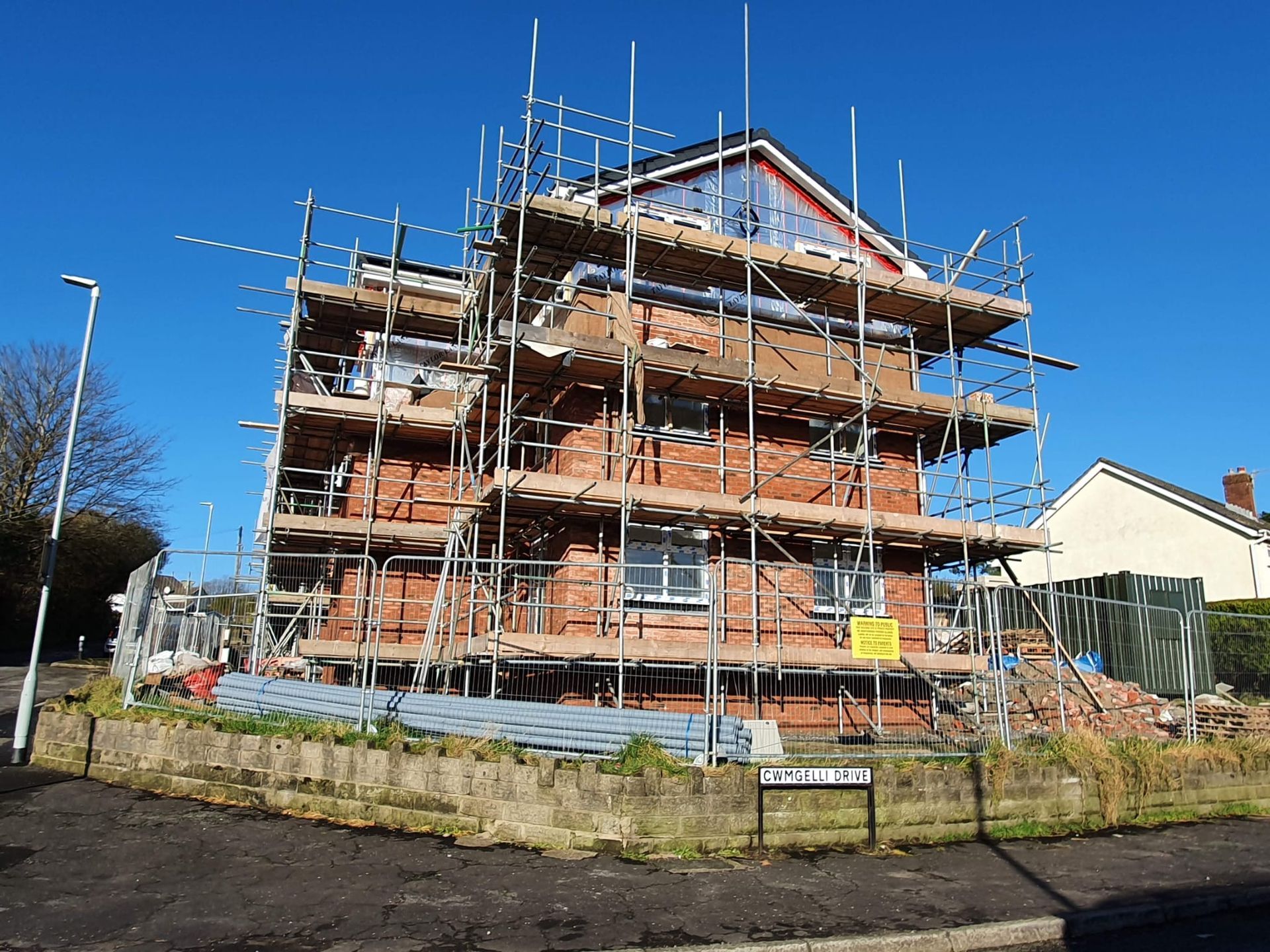 Brick house under construction with scaffolding on a sunny street corner