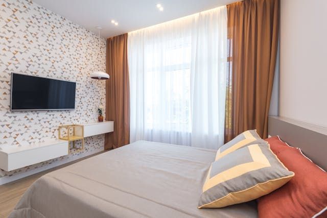 a bedroom with burnt orange curtains and grey sheets