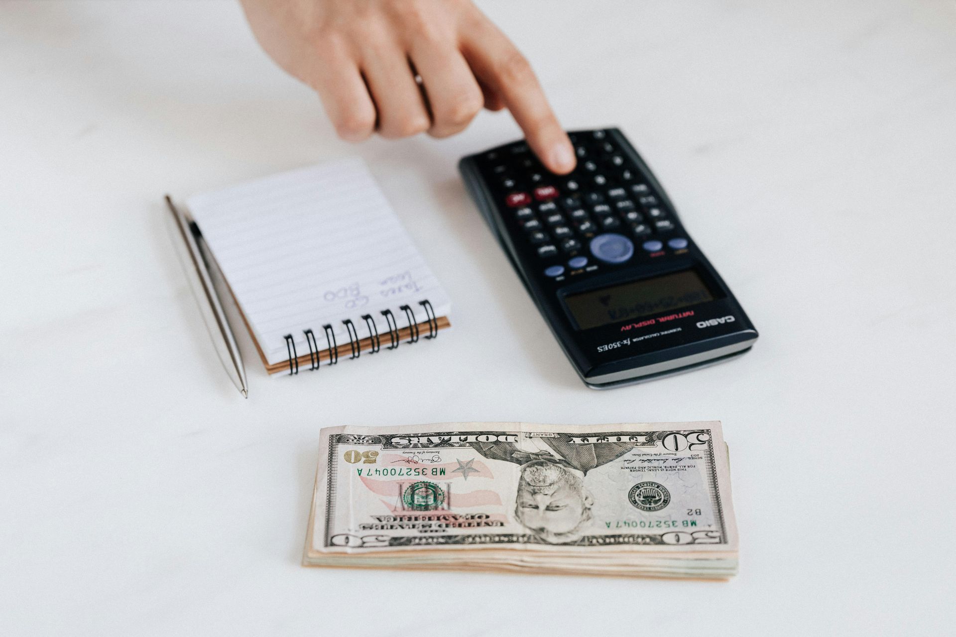 someone using a calculator next to a notepad and a pile of cash