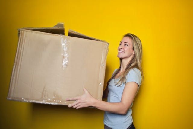 person carrying moving box with bright yellow background