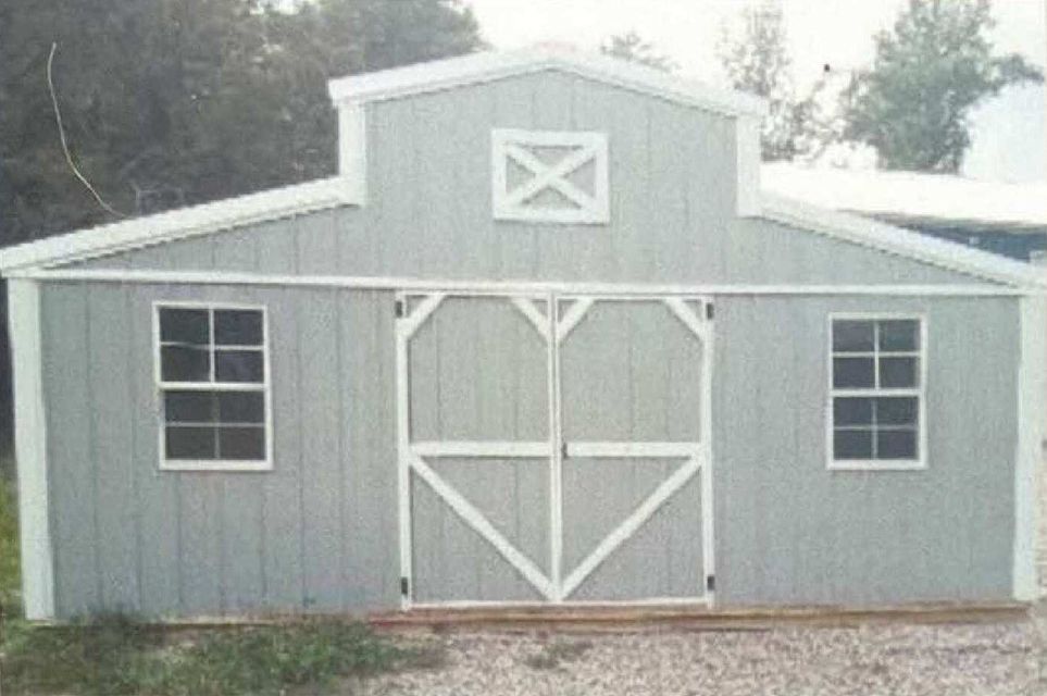 Light blue wooden barn with white trim and double doors, centered in a gravel yard.
