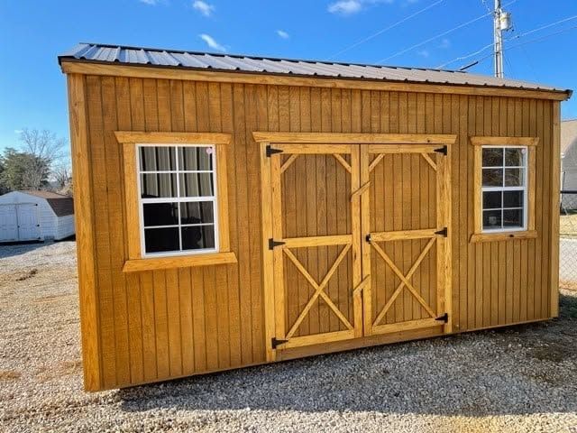 Wooden garden shed with double doors and two windows on a gravel lot under a blue sky