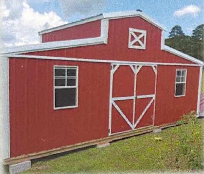 Red barn with white trim and doors on a grassy slope under a partly cloudy sky.