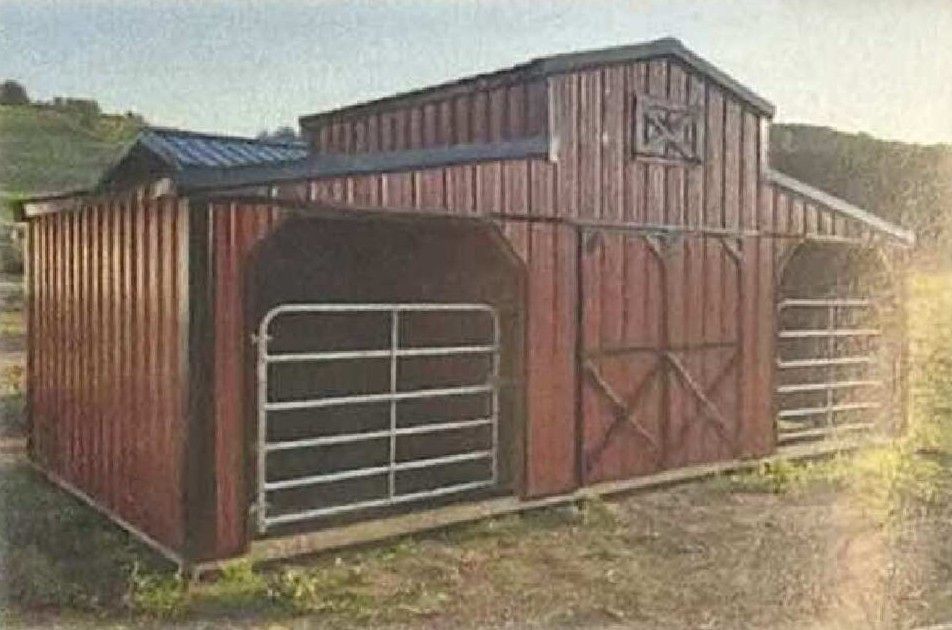 Red wooden barn with metal gates and a loft door in a grassy rural setting