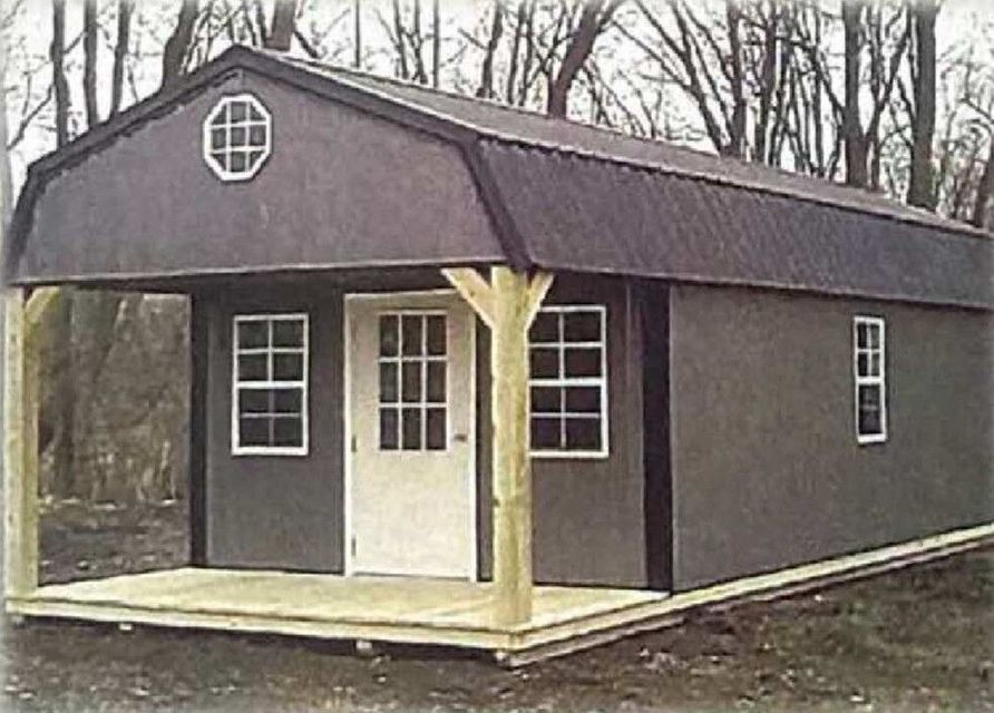Small dark cabin with white trim and porch in a wooded area