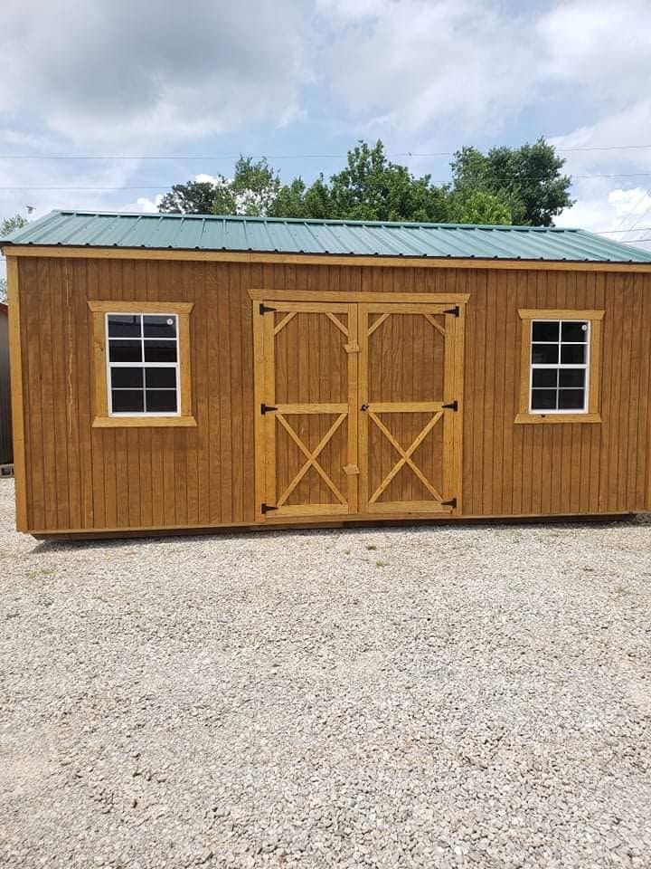 Wooden garden shed with green metal roof, double doors, and two windows on a gravel lot.