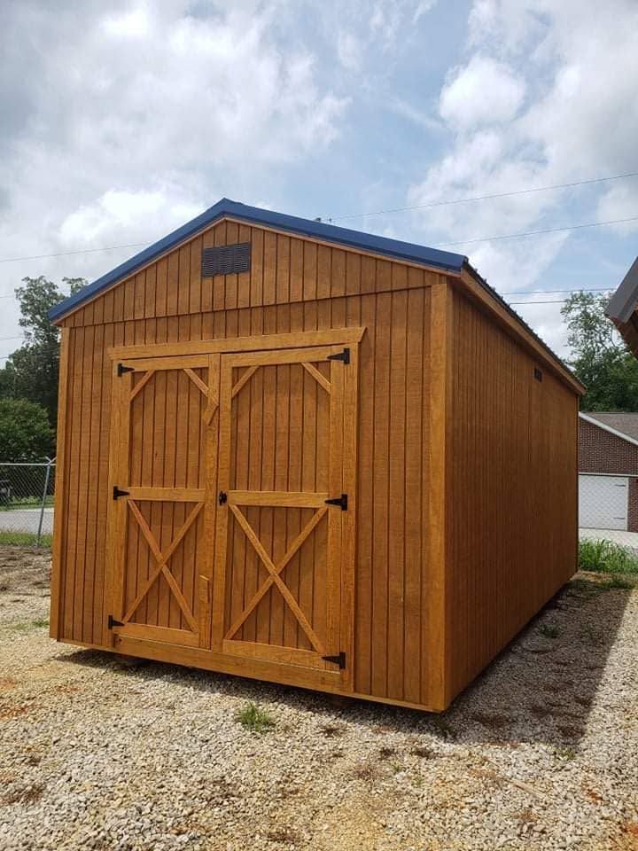 Wooden storage shed with double doors on a gravel lot under a cloudy sky