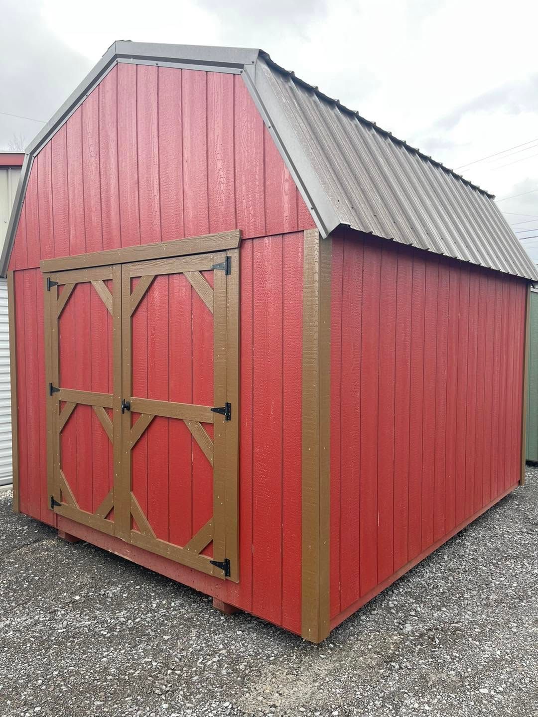 Red wooden garden shed with tan double doors and a gray metal roof on gravel.